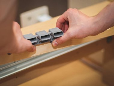 Kafkasyalı genç bir adamın elleri, tahta tahtalardaki bir yatak tabanına plastik bağlayıcılar yerleştiriyor, odasında yerde oturuyor, tarlanın derinliği ile yakın plan yan görüş. Mobilya montajı, alışveriş anlayışı, evde.