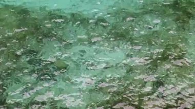 Beautiful view of the sea ripples of azure green water with visible stones at the bottom on a summer day in the south of France, close-up view from above in real motion.