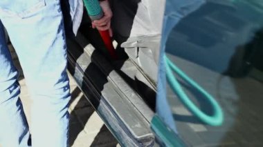 Beyaz tenli genç bir adam, güneşli bir bahar gününde açık bir araba yıkama yerinde arabasının iç koltuğunun altını vakumluyor..
