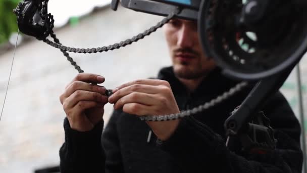 One young Caucasian man manually connects a bicycle chain to a bicycle while sitting in the backyard of the house, close-up side view. Bicycle repair concept.
