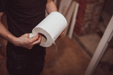 Siyah üniformalı beyaz bir erkek müteahhit elinde bir rulo kağıt havlu tutuyor, yakın çekim. Ev tadilatı, pencere montajı, inşaat işleri.