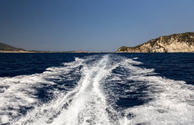 Güneşli bir yaz gününde mavi denizdeki bir teknenin motorunu kesen köpüklü dalgaların güzel bir manzarası bulanık kayalık bir adanın arka planına yakın bir kenar manzaraya karşı..