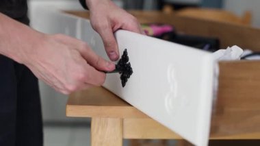 Beyaz tenli genç bir adam, beyaz bir çekmeceye saplı siyah bir kilit takıyor. Gün boyunca odada dikiliyor..