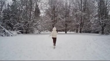 Beyaz ceketli, sırtında kapüşonlu ve kahverengi pantolonlu beyaz bir kız Belçika 'nın kış ormanlarında, yakın çekimde koşuyor. Kış tatili kavramı, modern