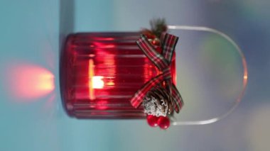 Mavi arka planda yanan bir mum alevi olan koyu kırmızı bir Noel kavanozu..