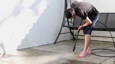 Koyu renk elbiseli esmer, beyaz bir adam bir yaz akşamı evinin küçük arka bahçesinde kirli bahçe fayanslarını yıkar ve eğilir..