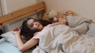 Saçları açık, küçük, beyaz tenli, güzel bir kız, sabah erkenden uyanıyor, elleriyle gözlerini ovuyor, yatakta uzanıyor, yakından bakıyor..