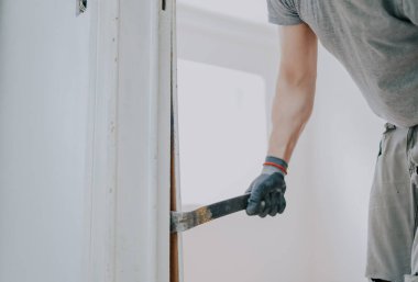Gri tekstil eldivenli genç beyaz bir adamın elleri, levye kullanarak eski ahşap çizgileri kapı aralığından seçici bir odaklanma ile kapatıyor. İnşaat işi kavramı..