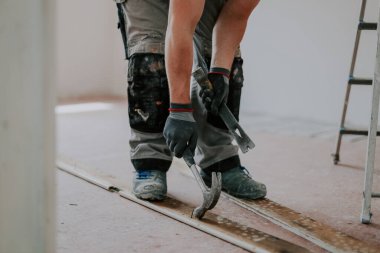 Üniformalı ve tekstil gri eldivenli genç beyaz bir adamın elleri sökülmüş eski ahşap kadifeden çivi ve levyeyle çivileri söküyor.