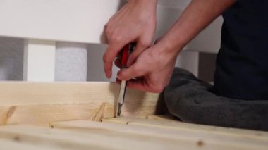 Tanınmayan bir genç tornavida kullanarak tahtaya vidasını manuel olarak vidalıyor. Bir yatak kurma kavramı, adım adım.