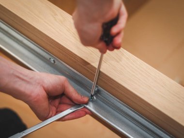 Kafkas bir gencin elleri, metal bir parçayı tahta bir yatağa bağlayan bir tornavidayla vidayı büküyor. Odasında yerde oturuyor, yakından bakıyor. Mobilya montajı kavramı