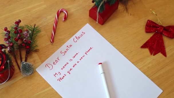 サンタクロースのための赤いフェルトチップペンで書かれた1つの手紙は 冬の日にダイニングルームでクリスマスの装飾と木製のテーブルの上に クローズアップトップビューがあります スローダウン — ストック動画