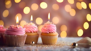 Pembe kremalı üç lezzetli kek, şeker serpintileri ve yanan mumlar masanın üzerinde bulanık bokeh ışıklarının arka planına karşı duruyor..