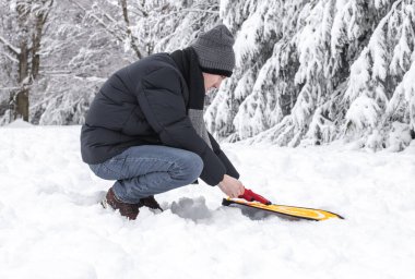 Mavi ceketli ve gri örgü şapkalı genç bir adam Belçika 'nın karlı bir orman arazisindeki karlı bir çayırda, yakın görüş alanında bir dron için sarı ped kuruyor. Kış kavramı
