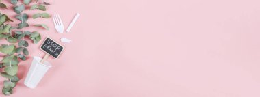 Beyaz plastik cam, kırık çatal, yazılı mandal: solda açık pembe bir zemin üzerinde duran plastiği ve yeşil dalları durdurun, sağda fotokopi alanı var, düz yakın plan. Konsept: