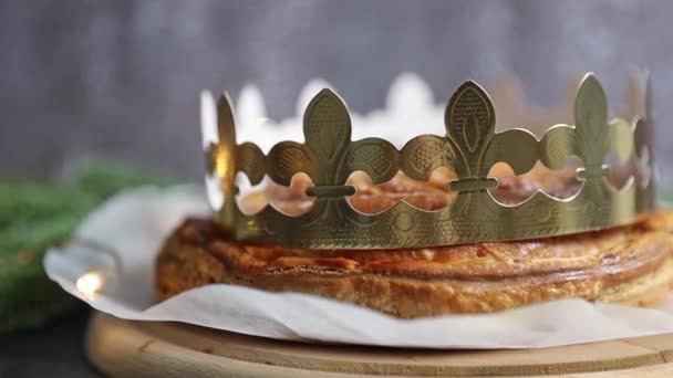 灰色の背景の上に黄金の冠が付いている一つの新鮮に焼かれた王室のガレット 選択的な焦点が付いている側面の眺めおよび右に追跡 — ストック動画