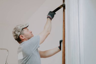 Üniformalı ve gri tekstil eldivenli genç beyaz adam eski ahşap kaideyi gözleri kapalı, alt tarafı seçici odaklı bir şekilde kaldırıyor. İnşaat işi.