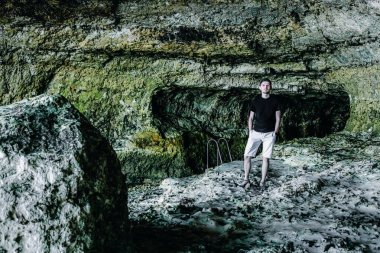 Siyah tişörtlü genç yakışıklı bir adam Fransa 'da tretat' ta sular çekildikten sonra bir su altı kaya mağarasında duruyor..