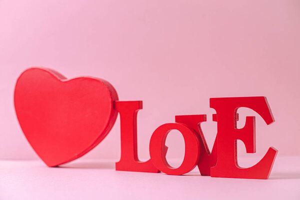 Red cardboard box and wooden solid word Love lie diagonally on a pink background, close-up top view. Valentines day concept.