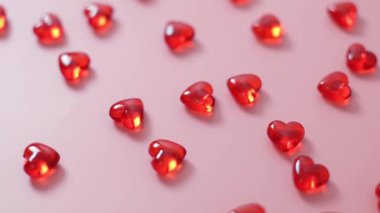 Pembe arka planda bir sürü küçük kırmızı cam kalp var, sağ tarafa doğru takip ediyorlar, yakın çekim alan derinliği ve seçici odaklanma ile birlikte. Aşk konsepti, Sevgililer Günü.