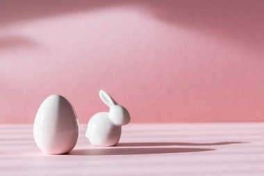 Paskalya yumurtası ve tavşanın porselen heykelcikleri solda, gölgeli pembe bir zemin üzerinde ve sağda fotokopi alanı, yakın plan..