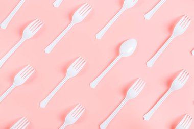Tek kaşıklı beyaz plastik çatallar pembe arka planda çapraz yatar, düz yakın plan yatar. Ekoloji konsepti, şablon, bayrak.