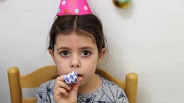 Kafasında kocaman kahverengi gözleri ve kafasında doğum günü külahı şapkası olan küçük beyaz bir kız kağıt boruyla ıslık çalıyor, masalara oturuyor, eğleniyor, yan gözle bakıyor.