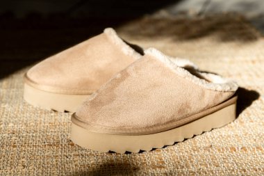 Bir çift modern modaya uygun, sıcak Uggs terlikleri yüksek bir platformun ortasında uzanır. Örülmüş bir halının üzerinde. Bir kış günü oturma odasının fayanslı zemininde.