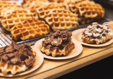 Taze Belçika waffleları karton çevre dostu tabaklarda çikolatalarla birlikte ahşap bir fırın vitrininde duruyor..