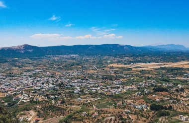 Güneşli bir yaz gününde, Rodos adasında, dağlara yakın bir ovada uzanan ve mavi gökyüzü olan bir köyün panoramik manzarası..