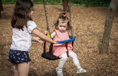 Kafkasyalı güzel bir esmer kızın portresi. Küçük kız kardeşini salıncakta sallıyor. Bir yaz günü parkta, çocuk parkında..