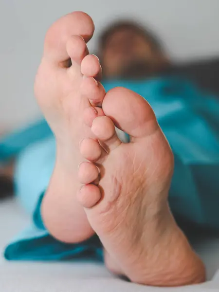 Clean and crossed feet of a young caucasian male patient in disposable pajamas lying on a bed with a blurred background, close-up side view. Body part concept.