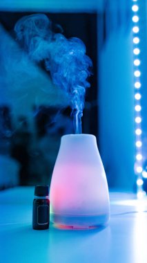 Bir pembe elektrikli oda parfümü ve bir şişe aromatik yağ. Neon ışığında bir güzellik salonunun masasında duruyor. Buharlaşan buhar ve aynada yansıması var..