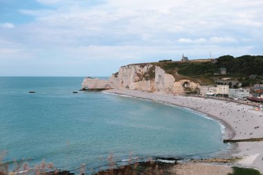 Kuzey denizinde doğal bir kemer olan setin güzel manzarası Etretat, Normandiya, Fransa 'da, bulutlu bir bahar gününde, insanlar kıyıda dinlenirken, yakın tepe manzaralı.