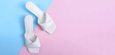 Bir çift beyaz kadın topuklu parmak arası terlik sol tarafta, arka planda mavi-pembe, fotokopi alanı ise düz yatağın sağında. Moda, güzellik, ayakkabı konsepti.