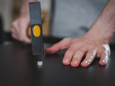 Beyaz, tanınmayan genç bir adam çekiçle siyah bir masa rafına beyaz plastik bir çekiçle vuruyor. Yerde, bir odada, tarlanın derinliği ile yakın çekimde oturuyor. Mobilya