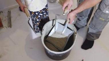 Tanınmayan genç bir Kafkasyalı müteahhit, küçük kızıyla birlikte çözeltiyi karıştırmak için metal kepçeyle bir kovaya kuru çimento döker.