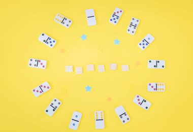 Renkli noktalı beyaz dominolar ve boş tahta küpler, merkezinde kopya alanı olan sarı bir zemin üzerinde daire şeklinde dizilir. Yaz tahtası oyun konsepti.