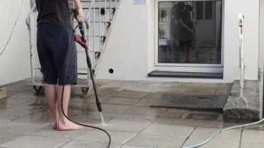 Genç, esmer, beyaz bir adam, bir yaz akşamı evinin arka bahçesinde duran bir Karcher makinesini kullanarak, çok kirli fayansları temiz su basıncıyla yıkıyor.