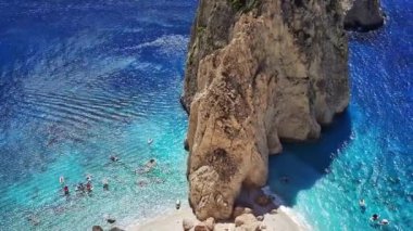 Yunanistan 'ın Zakynthos adasında güneşli bir yaz gününde, İyon Denizi' ndeki güzel bir kayanın gök mavisi suyu ve kıyıya demirlemiş teknelerle manzarası yukarıdan görülüyor.