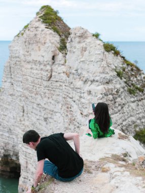 Arkadaki dağda oturan beyaz tenli genç bir çift etretat, Normandiya, Fransa 'da Kuzey Denizi' ni hayranlıkla seyrediyor..