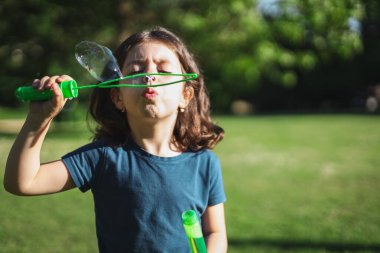 Beyaz tenli güzel bir esmer kızın portresi. Sabun köpüğü şişiriyor. Parkta beline kadar batmış duruyor. Parklar ve Rekreasyon kavramı, mutlu çocukluk.