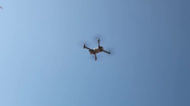 Güneşli bir yaz gününde mavi gökyüzünde küçük gri bir dron uçuyor, alttan yakından, yavaş çekimde. Teknoloji kullanma kavramı, modern yaşam tarzı.