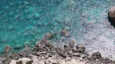 Güneşli bir yaz gününde, kıyıya yakın kayalık bir zeminde, yukarıdan zoom yaparak, temiz ve temiz bir su sıçratan güzel atmosfer manzarası. Seyahat zamanı konsepti, doğal