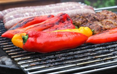 Seasonal red and yellow peppers fried on a grill with meat in the backyard of the house, close-up side view. Grill food concept.