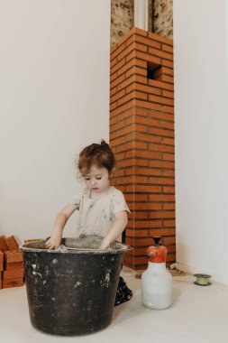 Küçük, güzel bir beyaz kız dizlerinin üstüne çöküp harcı spatulayla harç kovanına dolduruyor. Bir şömine için bir sigara içicisinin yenilenip yerleştirildiği bir odada.