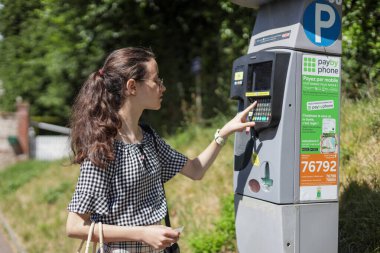 Etretat, Normandiya, Fransa - 26 Haziran 2022 - Güneşli bir yaz gününde park yerinin arkasında park sensörleriyle ödeme yapan güzel beyaz bir genç kızın fotoğrafı.