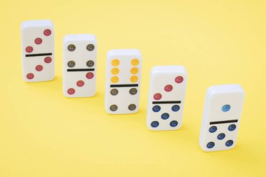 Beş beyaz domino taşının üzerinde renkli noktalar var. Sarı arka plan üzerinde köşegen şeklinde duruyorlar. Yakın plan düz. Yaz tahtası oyun konsepti.