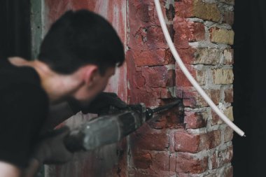 Siyah üniformalı beyaz bir adam, tuğla bir duvara yumruk atarak delik açıyor. Büyük bir tornavidayla, yakın çekim, seçici bir odak noktası var. Ev yenileme konsepti, inşaat işi.