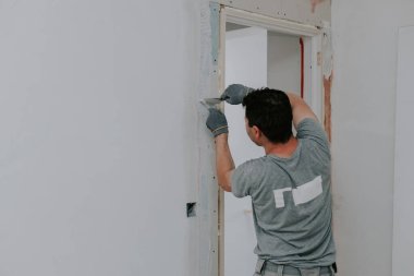 Gri üniformalı, beyaz tenli genç bir esmer ve eldivenler, kapının arkasında duran beyaz bir macunla, seçici bir odak noktasıyla binayı örterler. Ev yenileme konsepti